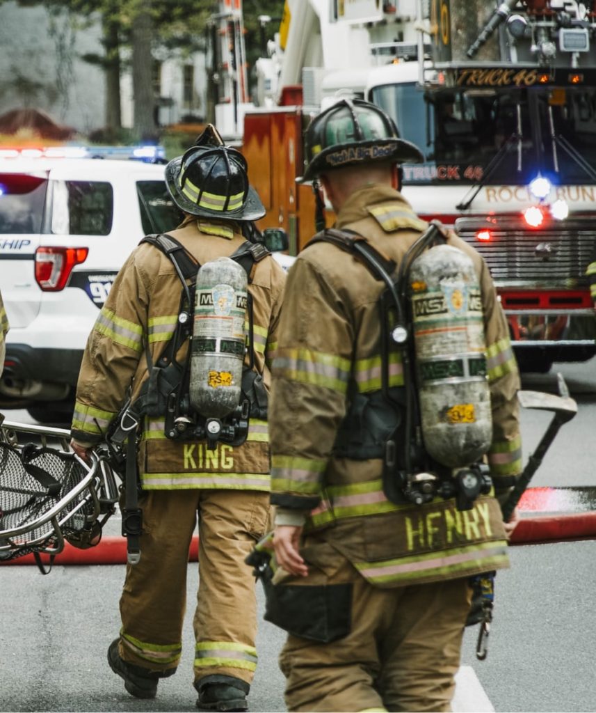 Firemen with gas tanks on there back carrying equipment in their hands