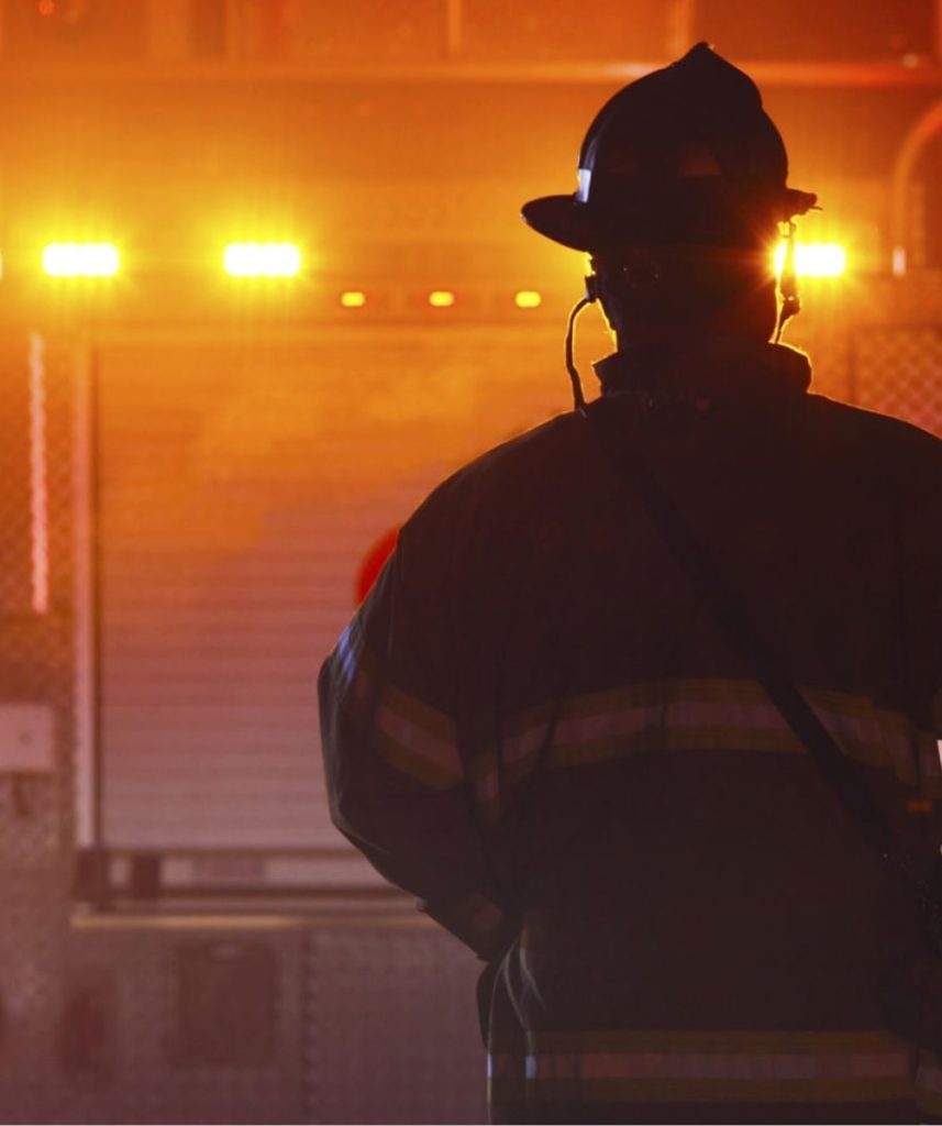 A silhouette of a firefighter in a helmet looking at the illuminated firetruck.
